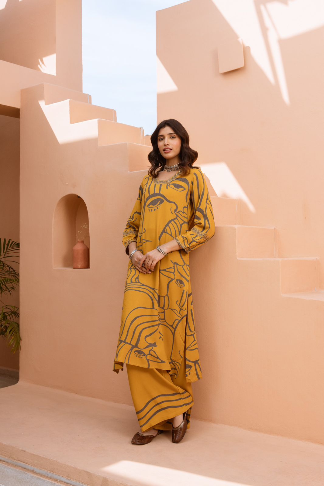 Woman in a yellow patterned outfit standing in front of a modern architectural structure.